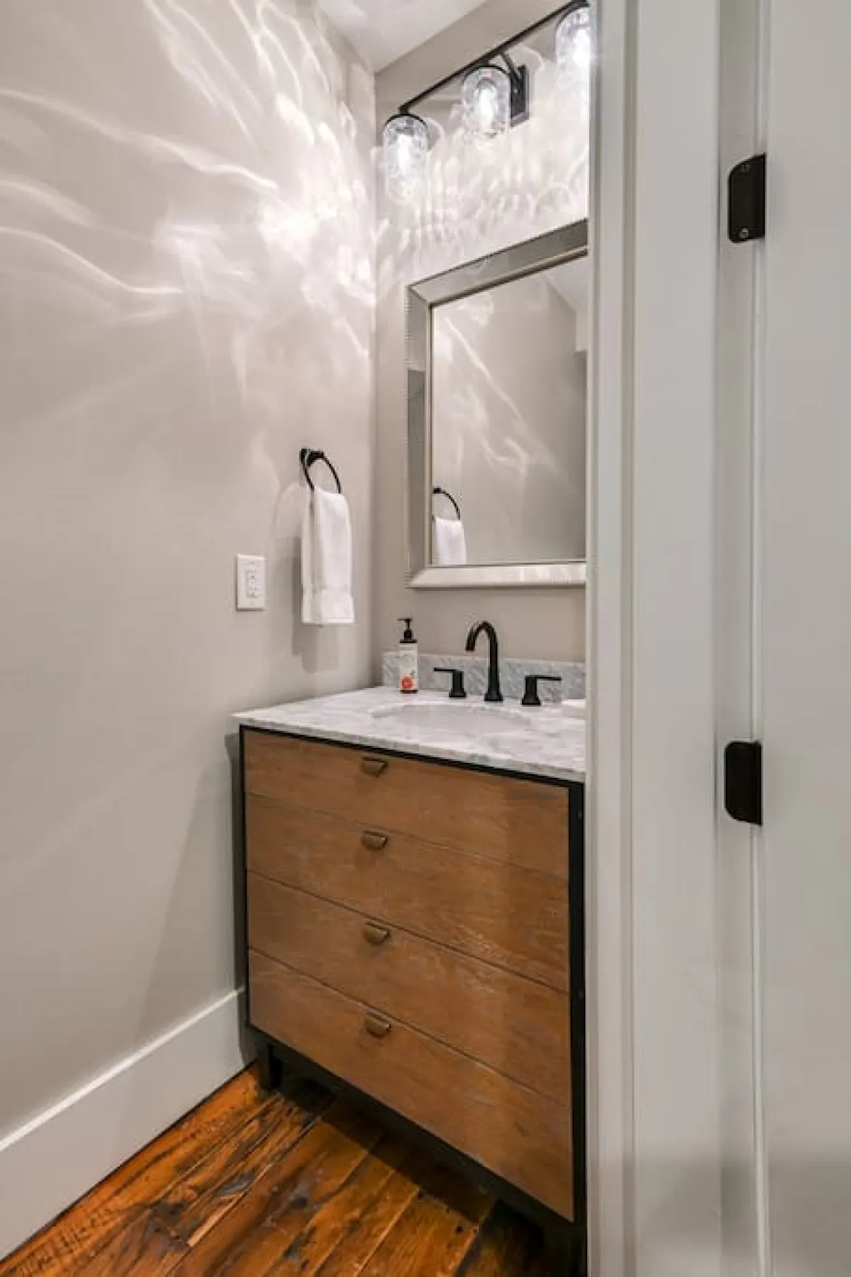 A modern powder room featuring a vanity with a marble countertop, a stylish mirror, decorative lighting, and wooden cabinetry. The clean, refined finishes echo the sophisticated urban vibe.