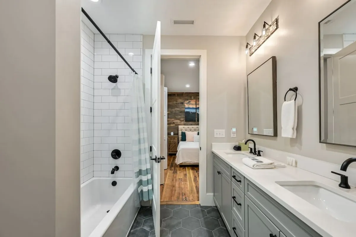 A modern bathroom with a double sink vanity, large soaking bathtub, and wood accent wall exudes calm and relaxation. The space is bright and inviting, designed for soothing baths or refreshing morning routines.