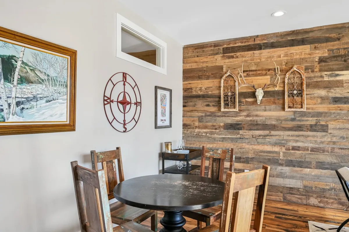 A warm dining area featuring a wooden accent wall, antler decor, a communal dining table, and vibrant artwork. The atmosphere is lively and social, mirroring the communal spirit of Asheville's downtown eateries and galleries.