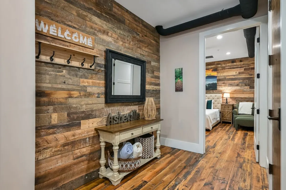 This image captures the entryway, featuring a welcoming sign, a console table, a mirror, and wooden wall accents. The warm flooring and inviting layout create a great first impression and set the tone for the home’s blend of original character and modern design.